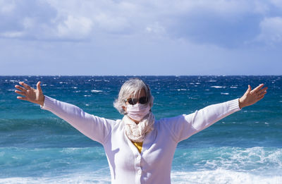 Portrait of senior woman with arms outstretched standing against sea