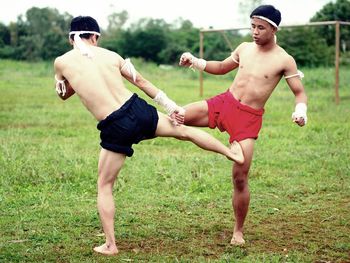 Shirtless male fighters practicing on grass against sky