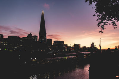 Illuminated buildings in city against sky at sunset