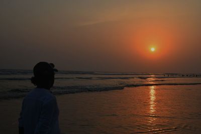 Rear view of man standing on beach during sunset