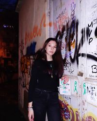 Portrait of young woman standing against graffiti wall