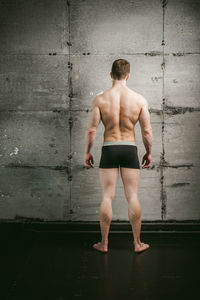 Rear view of shirtless muscular man standing by wall