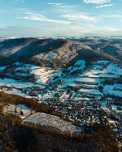 Hill with forest and snowy sunny fields behind village