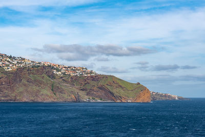 Scenic view of sea by mountain against sky