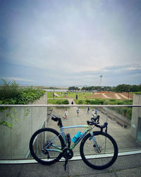 Bicycle parked by railing against sky