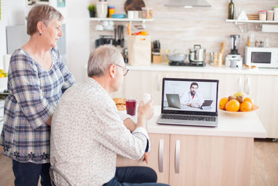 Rear view of man and woman using phone while sitting on table