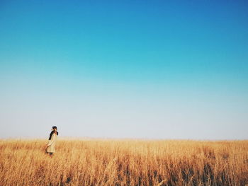 Rear view of woman standing on field against clear blue sky