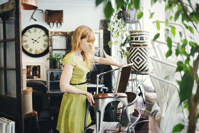 Mid adult woman stacking chairs in interior design shop