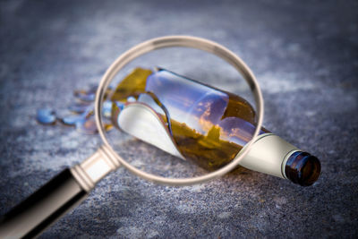 Close-up of magnifying glass by broken beer bottle on land