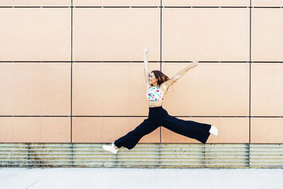 Full length of woman jumping against wall