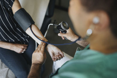 High angle view of physician checking blood pressure of woman in clinic