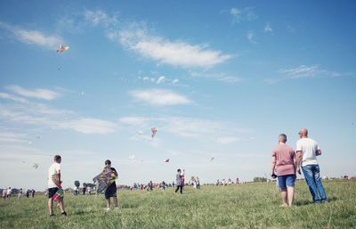 Rear view of people enjoying on field against sky