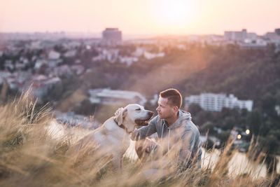Man sitting by dog on grassy field during sunset