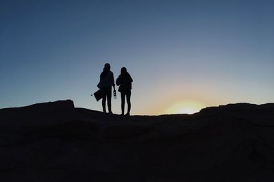 Silhouette friends standing on rock at sunset