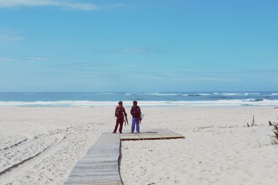 Rear view of people standing at beach against sky