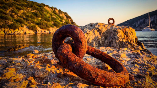 Close-up of rusty chain on riverbank against sky during sunset
