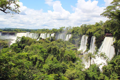 Scenic view of waterfall by trees against sky