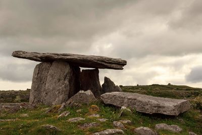 Cross on rock on field against sky