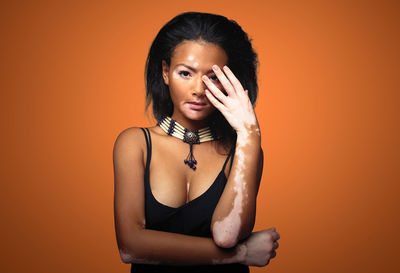 Portrait of young woman standing against orange background