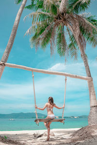 Beautiful girl on a swing between palm trees on the beach