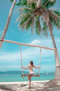 Rear view of woman sitting on beach against sky