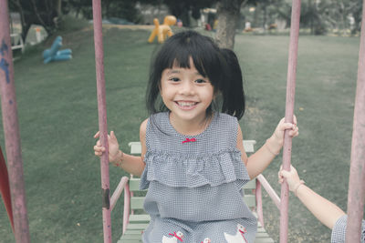 Portrait of smiling girl sitting on swing at park