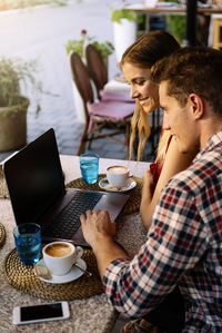 Couple using laptop while sitting at sidewalk cafe