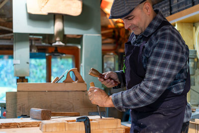 Side view woodworker with wooden hammer and chisel carving wooden detail while working in professional joinery workshop