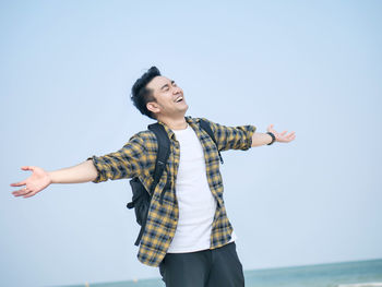 Smiling man with arms outstretches standing against clear sky