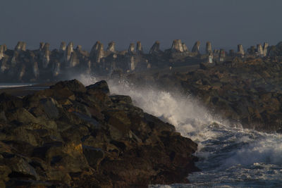 Waves splashing on rocks against clear sky