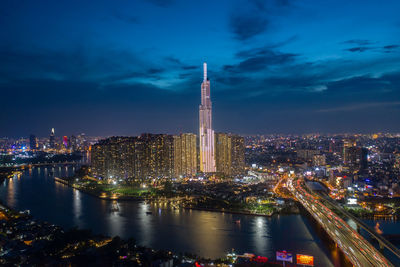 Illuminated city by river against sky at night