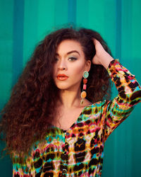 Close-up portrait of young beautiful woman with hand in hair against green corrugated iron