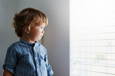 Boy looking away while standing against wall at home