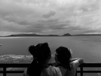 Rear view of sisters standing by sea against cloudscape