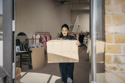 Female owner carrying cardboard box walking towards door in clothing store