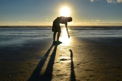 Silhouette of people standing on beach at sunset