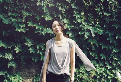 Portrait of smiling young woman standing against plants