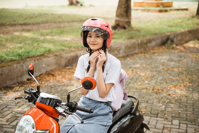 Side view of young woman holding hardhat while sitting on street