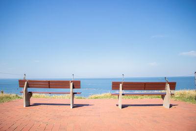 Empty bench on beach against blue sky