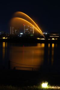 Illuminated city by river against sky at night