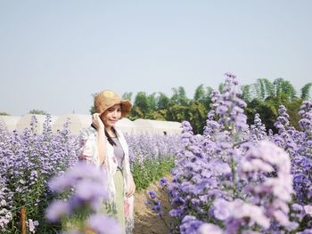 Woman standing on purple flowering plants on field against sky