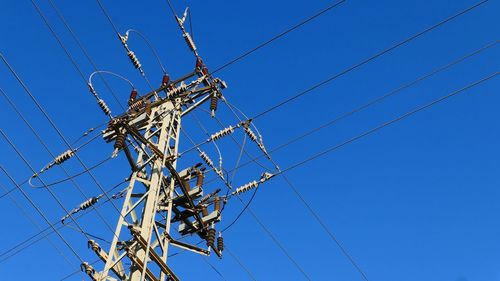 Low angle view of electricity pylon against blue sky