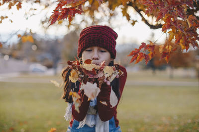 Cute girl blowing autumn leaf at park