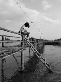 Woman sitting on pier at lake against sky