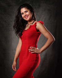 Portrait of smiling young woman standing against black background