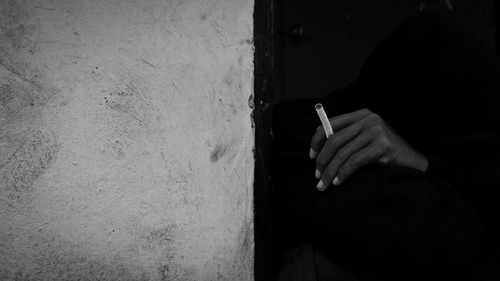 Midsection of man smoking cigarette against wall