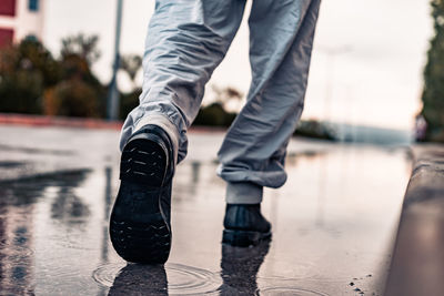 Low section of man walking on wet road during rainy season
