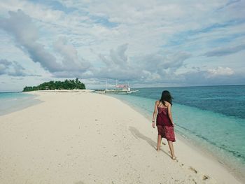 Rear view of woman walking on beach against sky