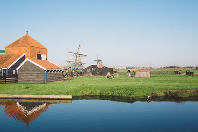 Traditional windmill by houses at lakeshore against sky