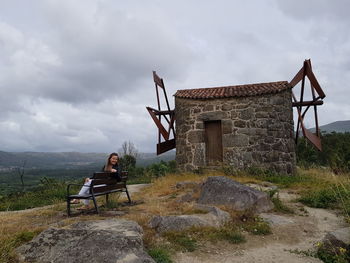 Man sitting on bench by rocks against sky